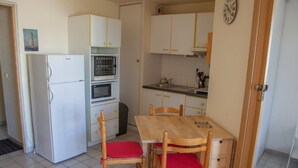 A compact kitchen with a refrigerator, oven, microwave, and a dining table with chairs.