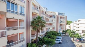 A multi-story residential building with balconies, a parking area, and greenery.