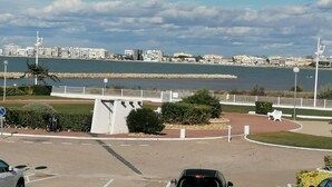 A coastal cityscape with a marina, a white monument, and a clear sky.