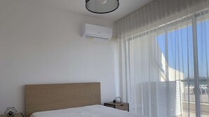 A bedroom with a wooden headboard, a white bedspread, a nightstand with a lamp, and a window with sheer curtains.