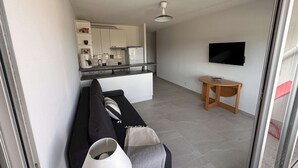 Una sala de estar moderna con un sofá, una mesita, un televisor y una cocina al fondo.