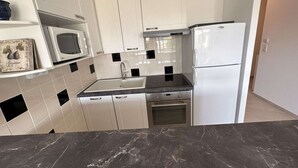Una cocina con armarios blancos, encimera negra, microondas, refrigerador y estufa.