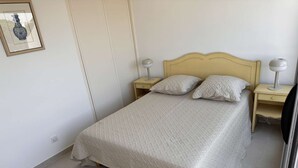 Una cama bien hecha con cubrecolcha acolchado, dos mesitas de noche con lámparas y un cuadro en la pared.