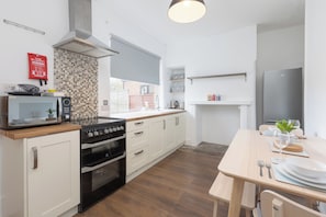 Une cuisine moderne avec des meubles blancs, une cuisinière noire, un four à micro-ondes et un coin repas comprenant une table et des chaises en bois.