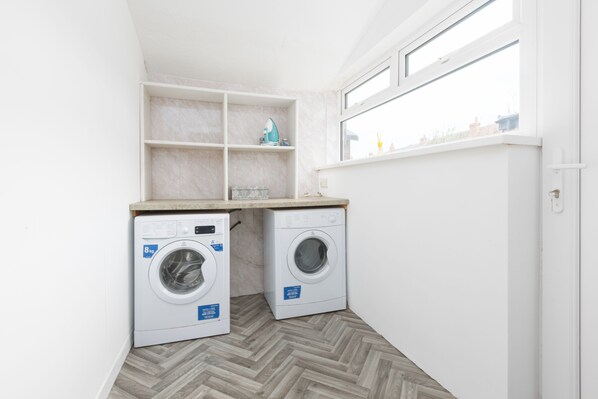 A compact laundry room with two washing machines, a wooden countertop, and a window providing natural light.
