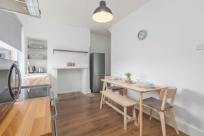 Uma cozinha compacta com área de refeições, piso de madeira, um banco e um relógio na parede.