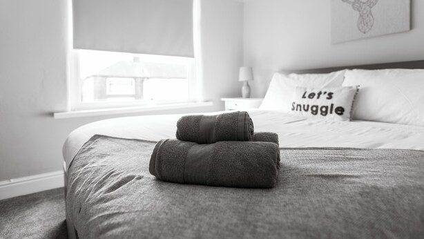 A neatly made bed with rolled towels, a pillow with the text "Let's Snuggle," and a deer head artwork on the wall. - Ansdell House, Ansdell Road (Blackpool)