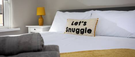 A neatly made bed with a pillow that reads "Let's Snuggle."