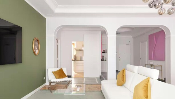 Ein modernes Wohnzimmer mit einem weißen Sofa, einem Glastisch und einer grünen Akzentwand.