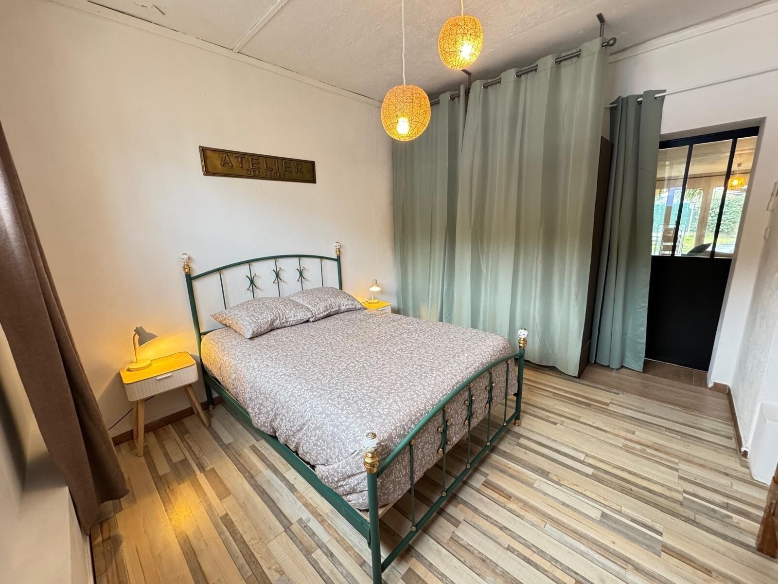 A bedroom with a bed, a nightstand, a wall-mounted sign, and a window with curtains.