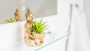 En gylden Buddha-statue holder en potteplante, placeret på en reflekterende overflade.