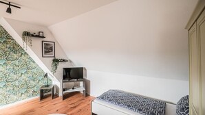 Et moderne loftværelse med skrå vægge, indbygget TV, hvid sofa og trægulv.