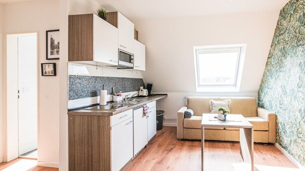 En kompakt opholdsstue med et tekøkken, en sofa og et spisebord.