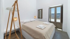 Een slaapkamer met een bed, een houten droogrek, een raam met uitzicht en een wandlamp.