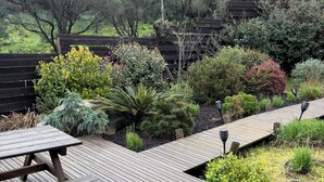 Een houten terras met een picknicktafel, omringd door verschillende struiken en planten.