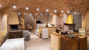 A rustic kitchen with a brick ceiling, a hanging chair, a dining table, and a bar area with a lamp. - Charming brick and stone loft in a 17th-century chapel in the historic center (Spello)
