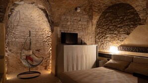 A room with a stone wall, a hanging chair, a bed, and a television. - Charming brick and stone loft in a 17th-century chapel in the historic center (Spello)