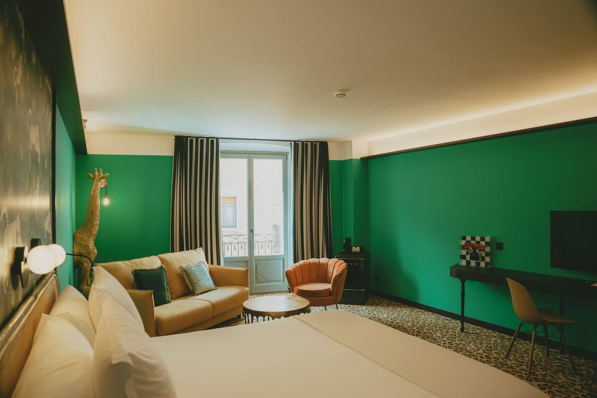 A hotel room with a bed, a sofa, a chair, a desk, and a giraffe statue.