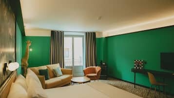 A hotel room with a bed, a sofa, a chair, a desk, and a giraffe statue.