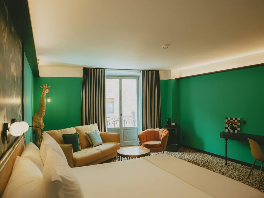 A hotel room with a bed, a sofa, a chair, a desk, and a giraffe statue.