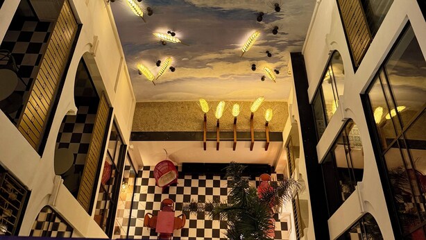 A hotel atrium with a checkered floor, a central chandelier, and a ceiling mural with a golden sphere and wheat stalks. - Hotel Divino by Fimedhotels (Figueres)