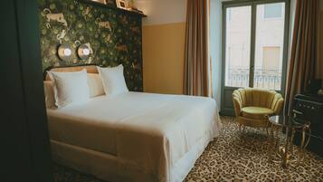 A hotel room with a bed, a chair, a table, a window with curtains, and a leopard print carpet.