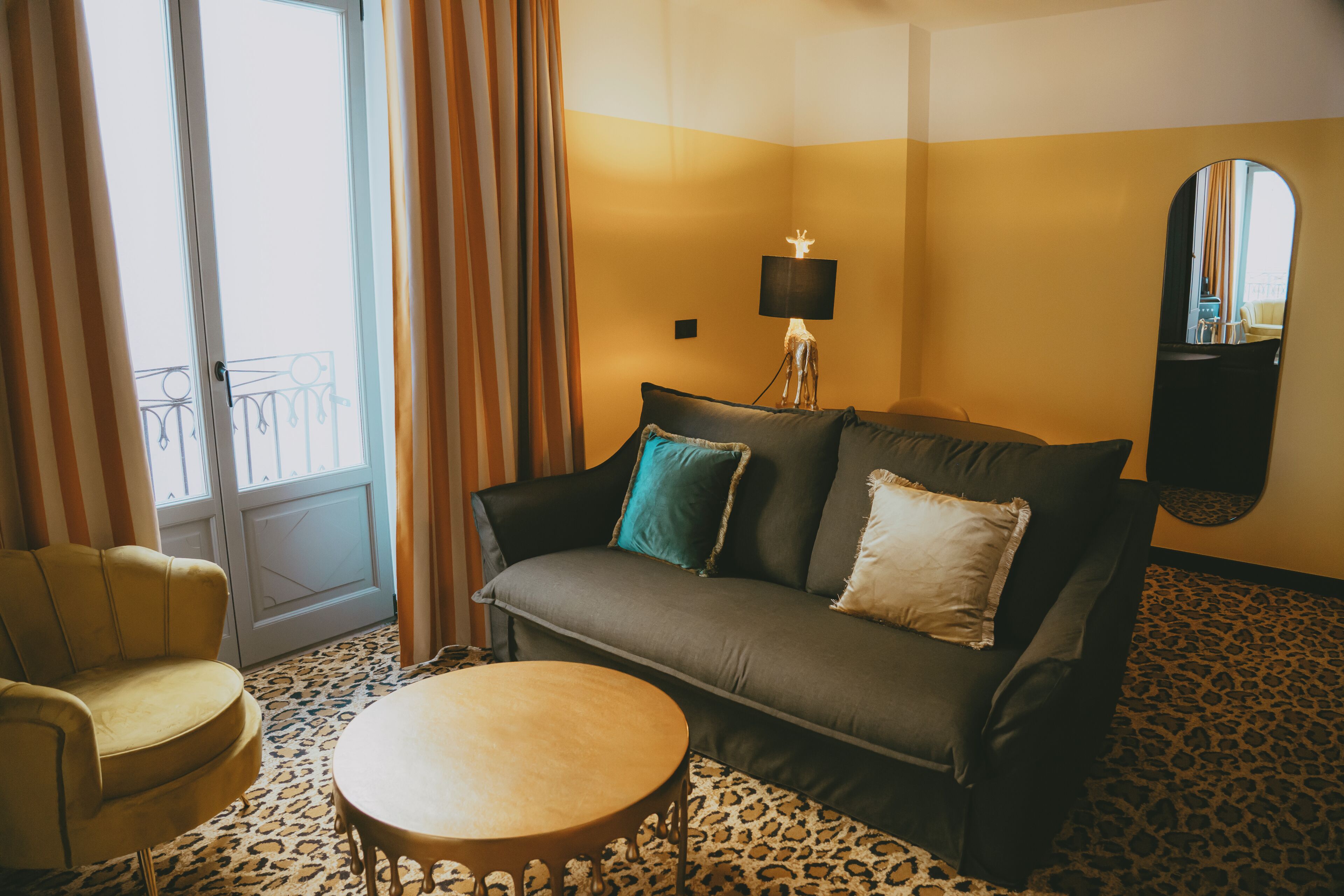 A room with a sofa, a round table, a lamp, a mirror, and a patterned floor.