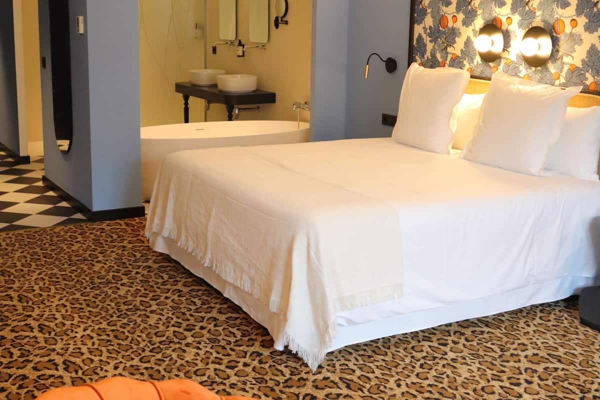 A hotel room with a bed, a bathroom with a sink and mirror, and a leopard print carpet.