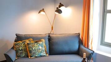 A room with a blue sofa, a leopard print carpet, a glass table with a bottle and glasses, and a window with orange curtains.