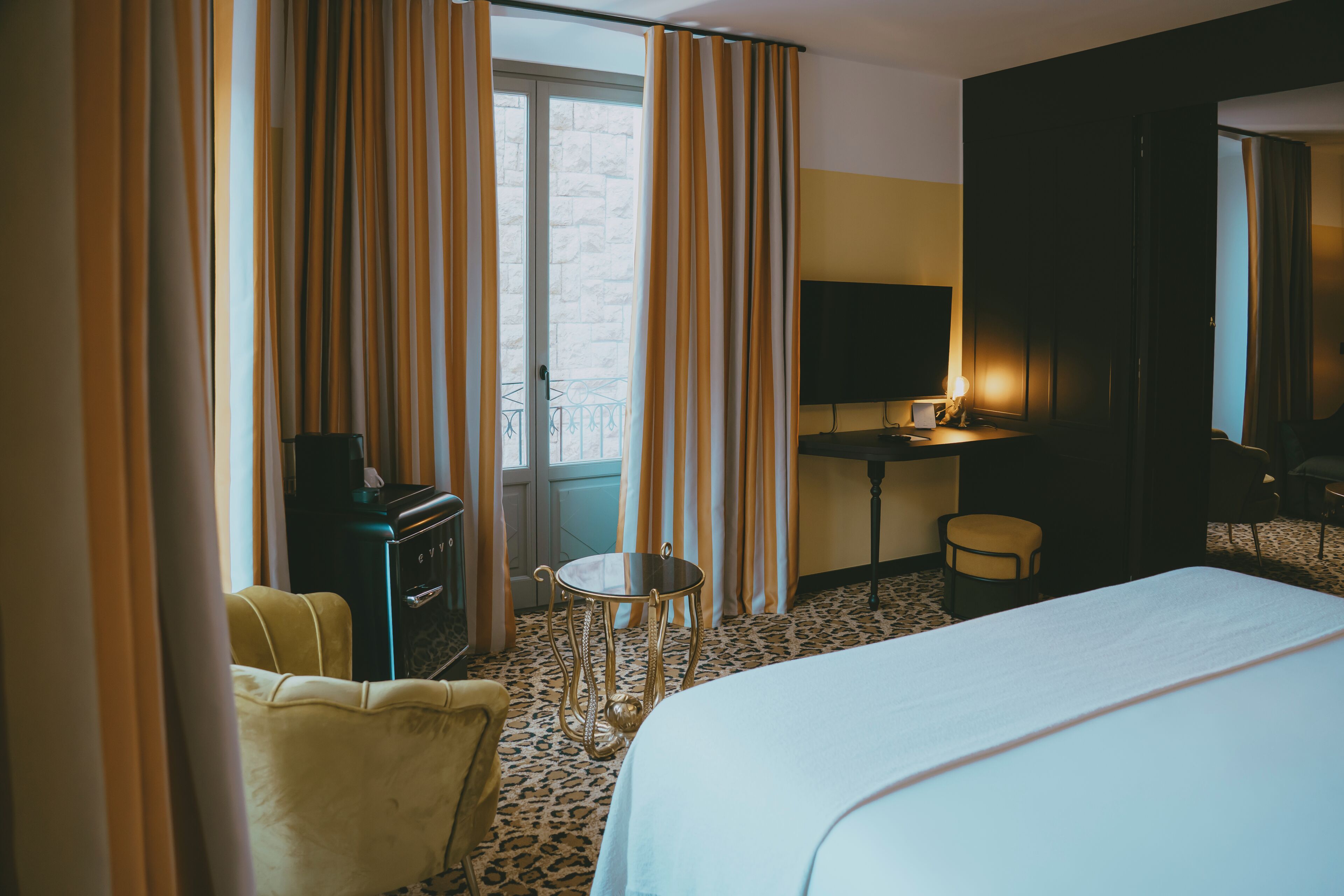Una habitación de hotel con cama, escritorio, silla, una mesita y cortinas.