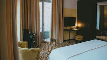 Una habitación de hotel con cama, escritorio, silla, una mesita y cortinas.