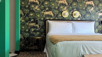 A hotel room with a bed, a small table, a chair, a patterned carpet, and a wall with a jungle-themed wallpaper.