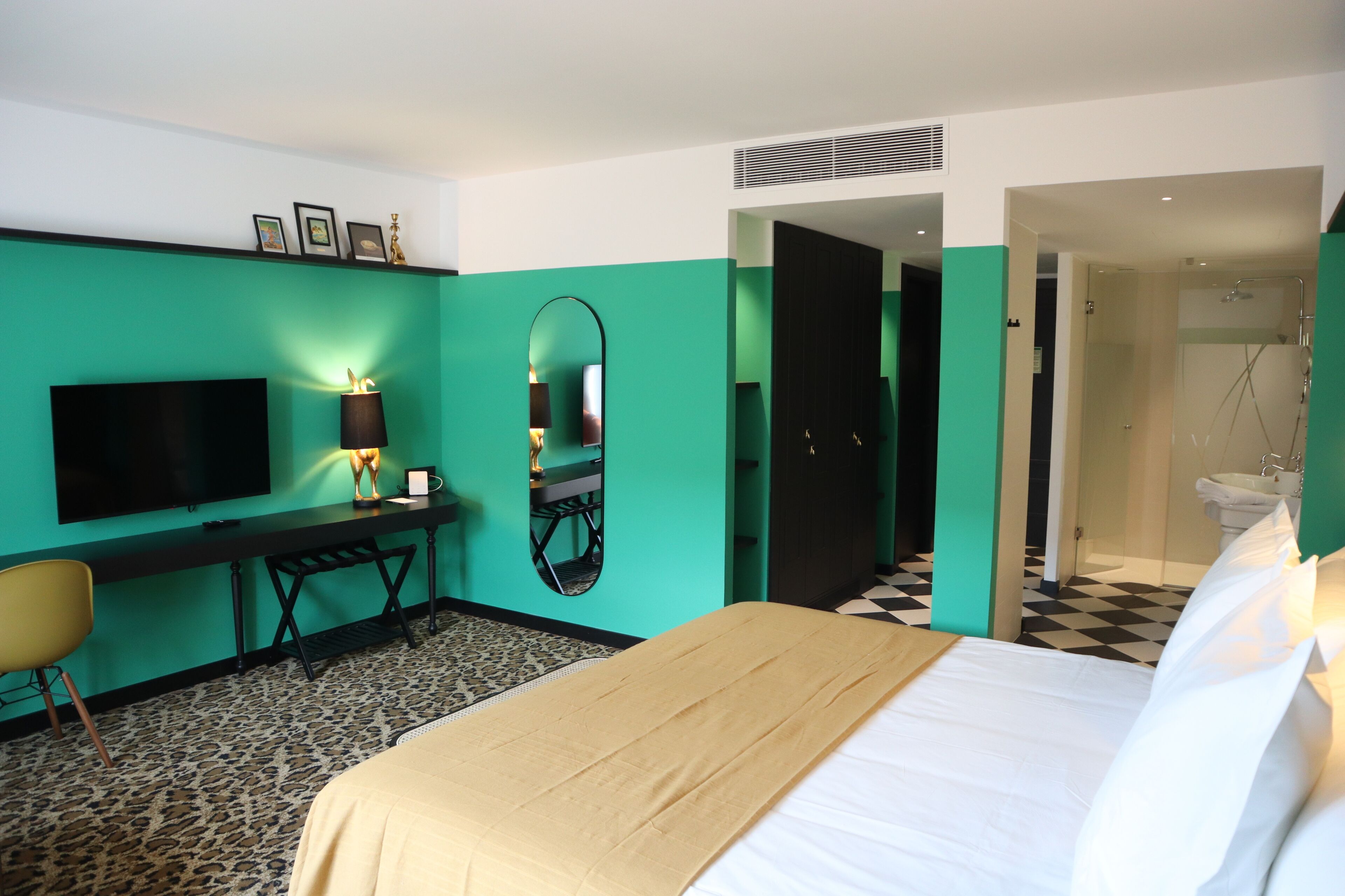 Een hotelkamer met een bed, een bureau, een televisie, een spiegel en een badkamer, zichtbaar door een geopende deur.