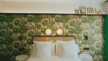 Un dormitorio con una cama, dos lámparas de noche, una estantería con fotografías y un papel tapiz de temática selvática.