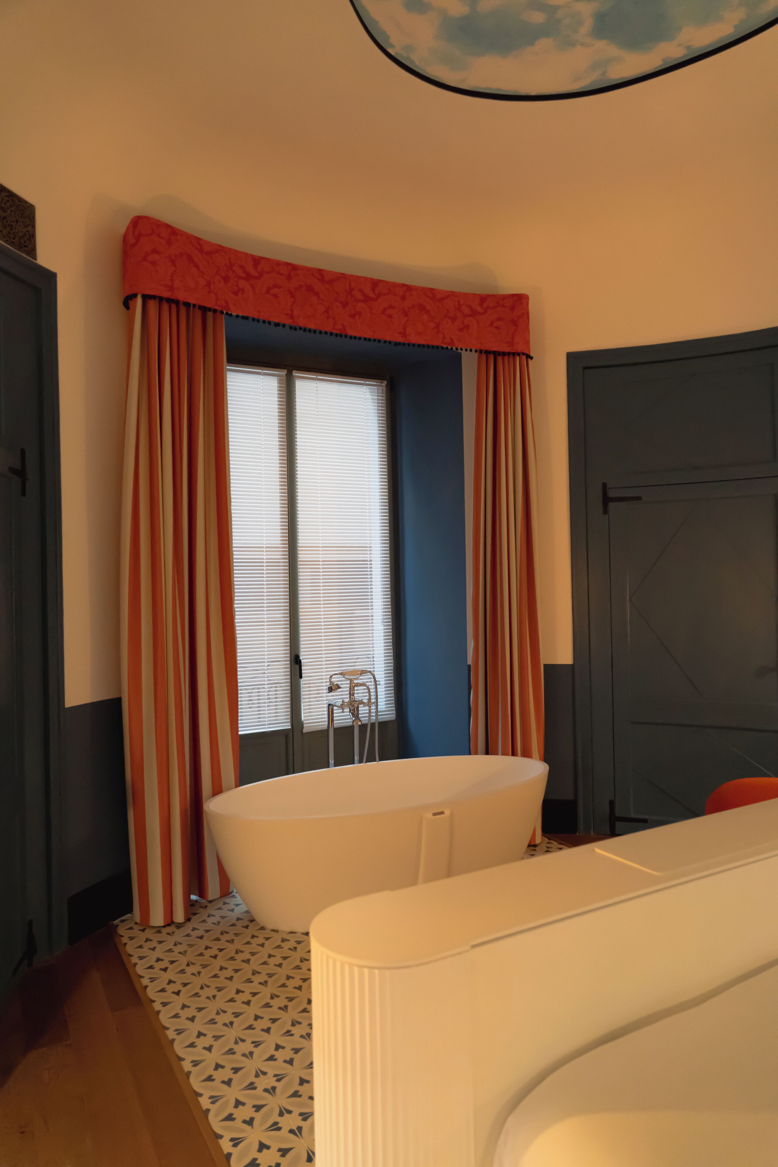 Un baño con bañera, ventana con cortinas, radiador y puerta.