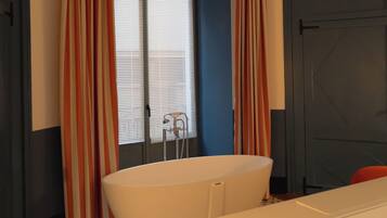 A bathroom with a bathtub, a window with curtains, a radiator, and a door.