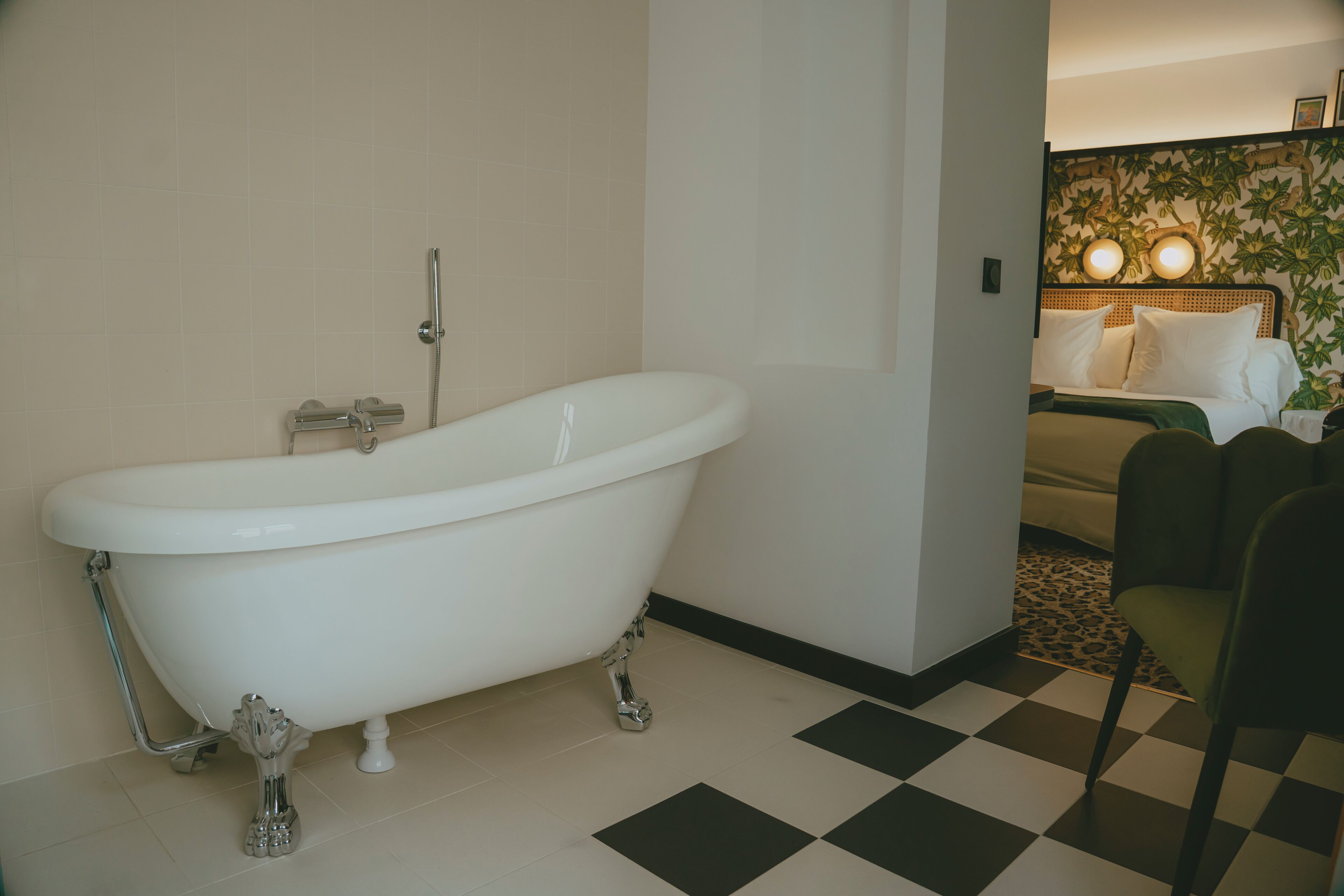 Una habitación con una bañera blanca tipo pata de león, suelo a cuadros y una cama con cabecera estampada.