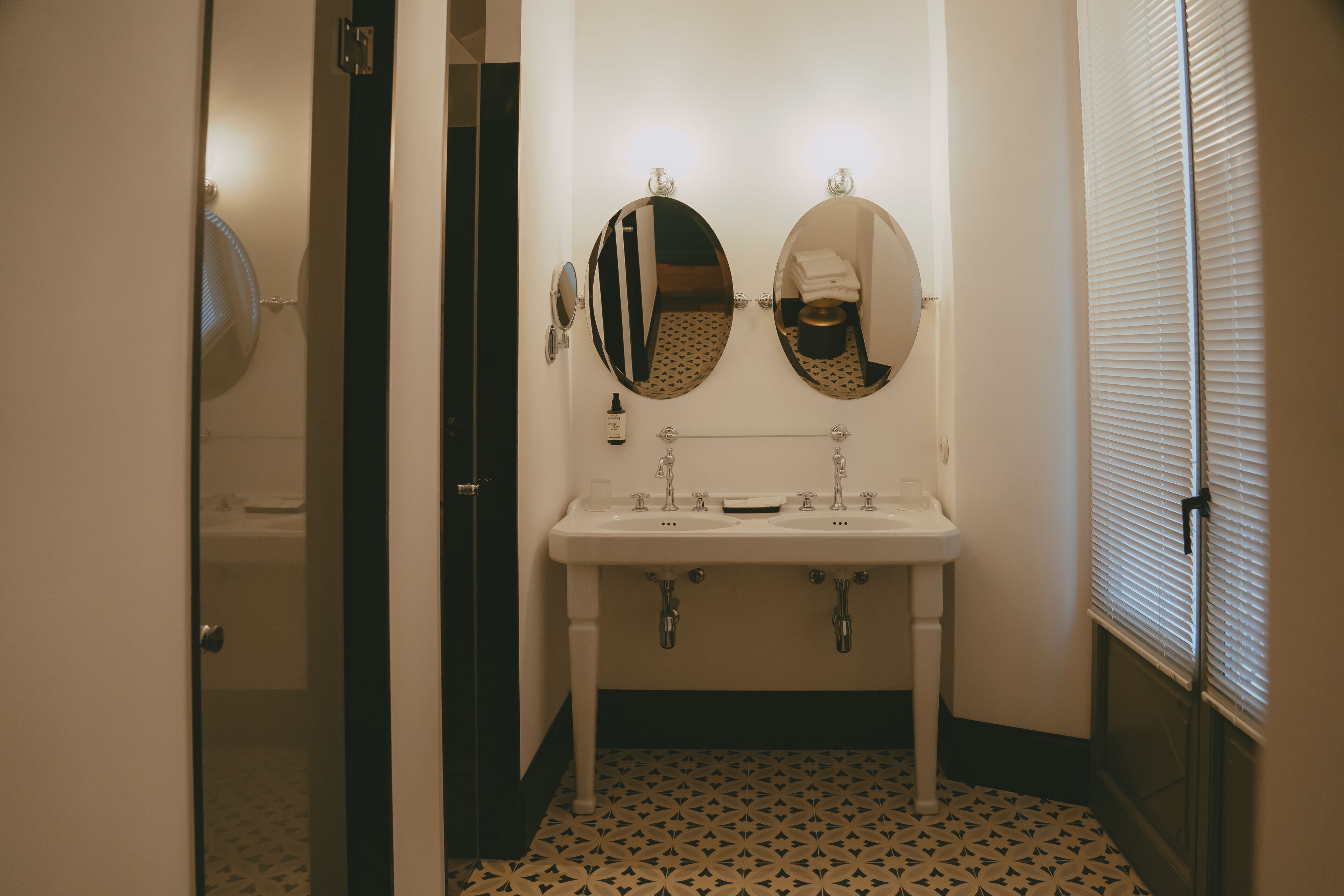 A bathroom with a white sink, two mirrors, and a patterned floor.
