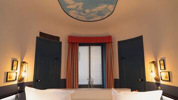 Habitación de hotel con cama, dos puertas, ventana con cortinas, luces fijadas en la pared y techo con diseño de nubes.