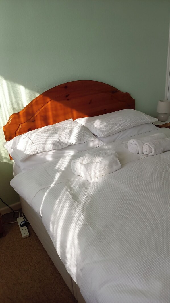Una cama bien hecha con sábanas blancas y cabecera de madera.