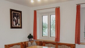 Ein Essbereich mit Holztisch und Bank, einem gerahmten Bild an der Wand und Fenstern mit roten Vorhängen.