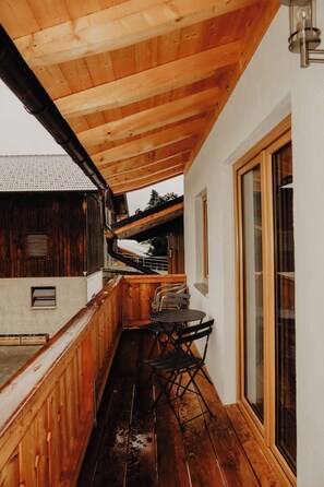 Un balcone in legno con tavolo e sedie, un soffitto in legno e un'ampia finestra.
