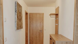 Ein schmales Gang mit einer Holztür am Ende, einem kleinen Schrank mit Schubladen und einem an der Wand befestigten Regal.