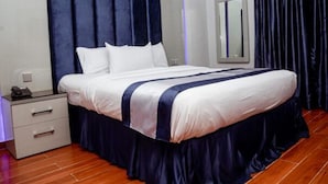 A modern hotel room with a large bed, a bedside table, a mirror, and dark curtains. - Novatel Hotel (Lekki)