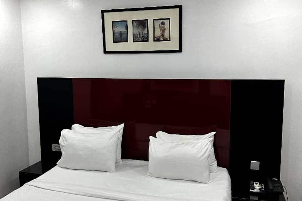 A hotel room with a large bed, a dark headboard, and a framed picture above the bed.