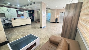 A reception area with a reception desk, a clock, a pillar with a sign, a trash bin, and a couch. - Novatel Hotel (Lekki)