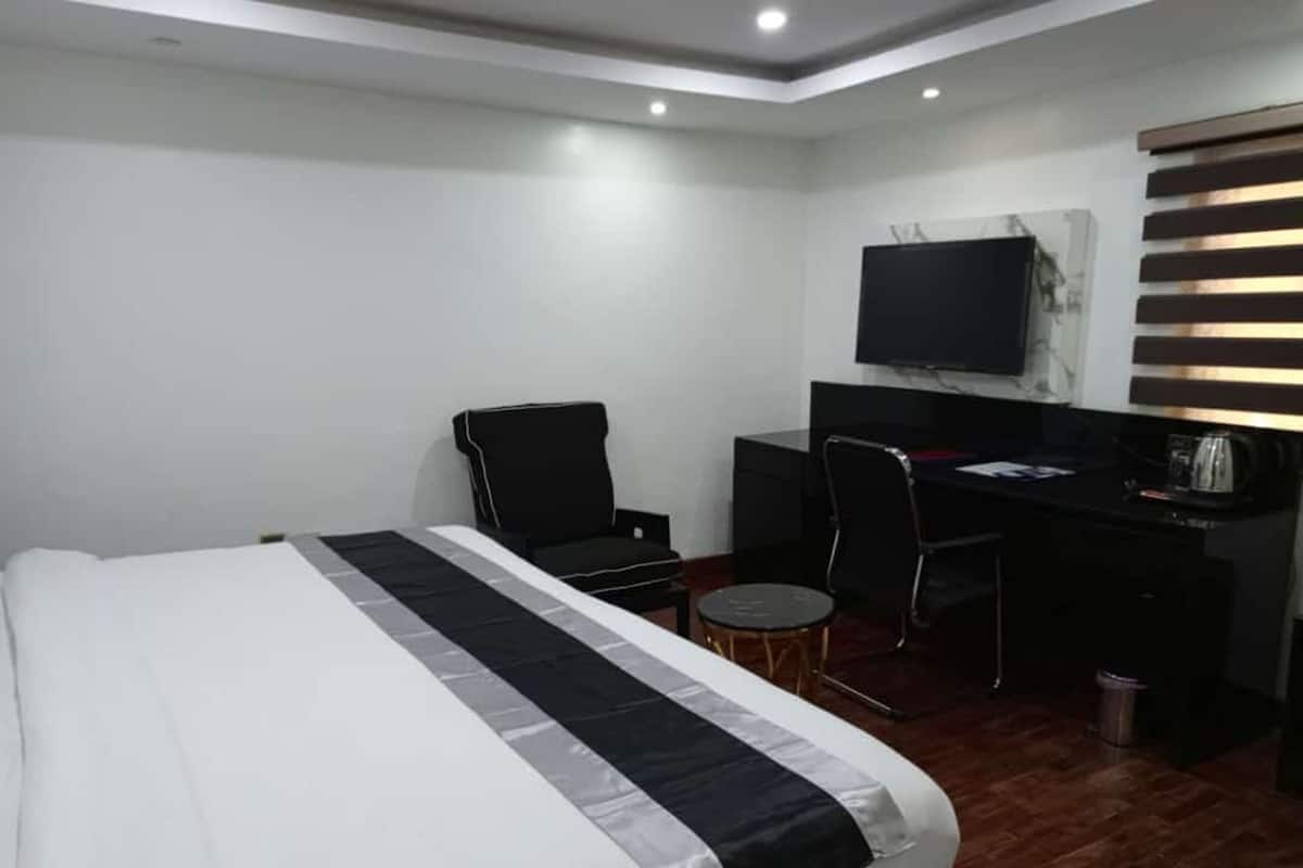 A hotel room with a bed, a desk, a chair, a television, and a small table.
