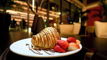 A dessert plate with a croissant and strawberries on a table in a dimly lit indoor setting.
