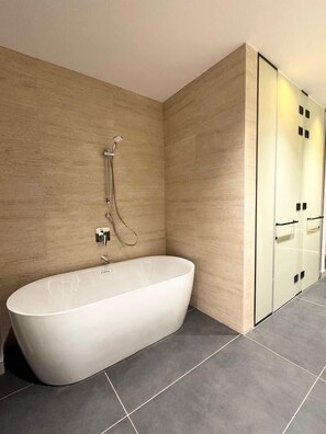 A modern bathroom with a freestanding bathtub, a glass shower enclosure, and a wooden wall. - Swisstouches Hotel Amman  (Amman)