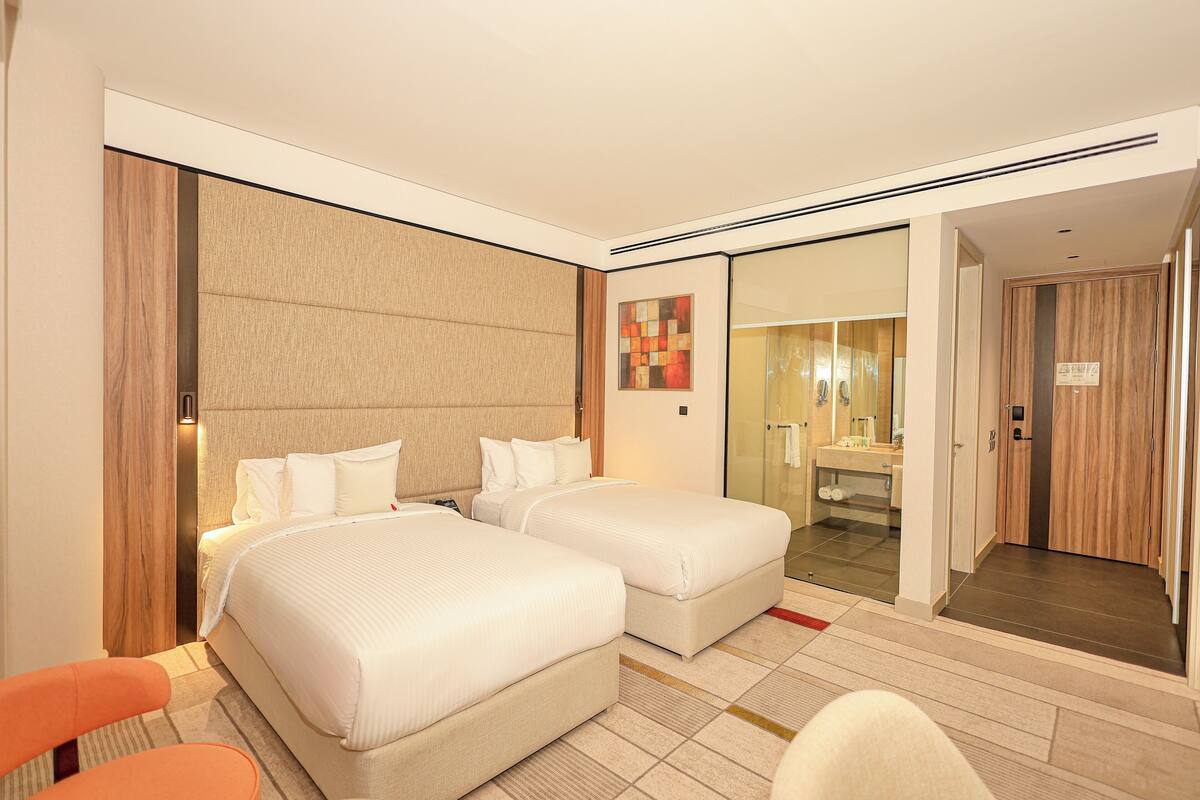 A hotel room with two beds, a bathroom, and a view of the hallway.